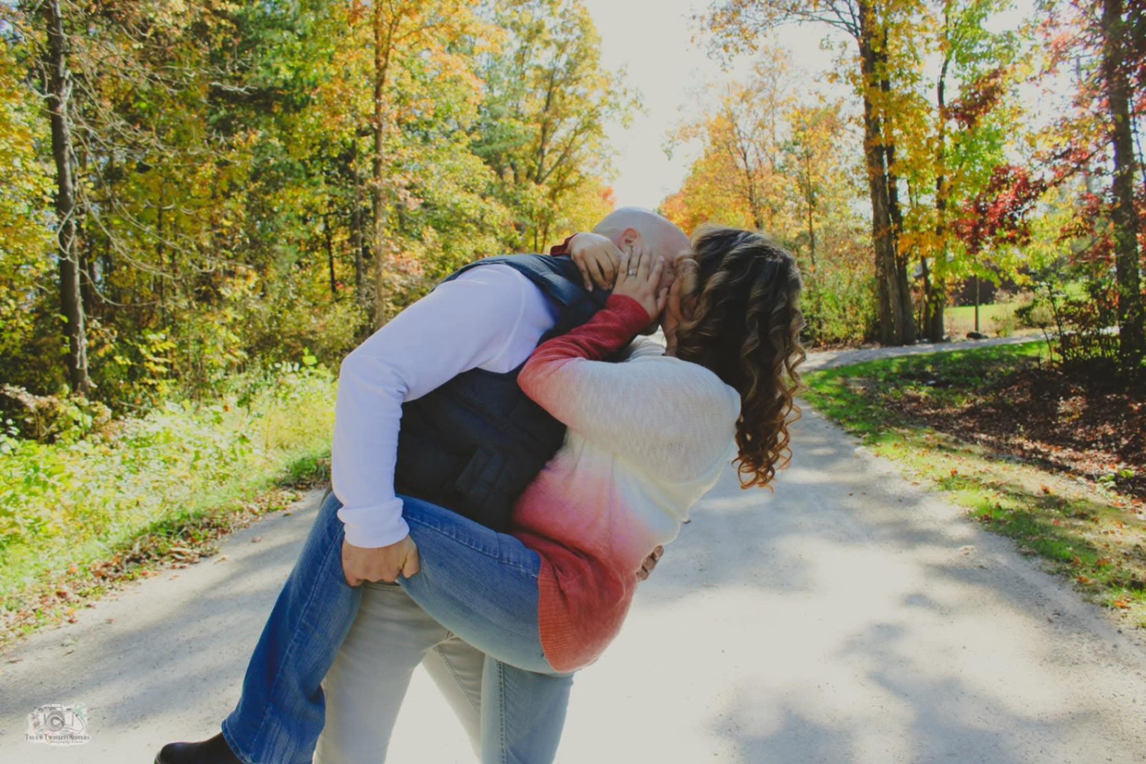 Couple sharing a romantic dip-kiss on a gravel path lined with autumn trees in full fall color
