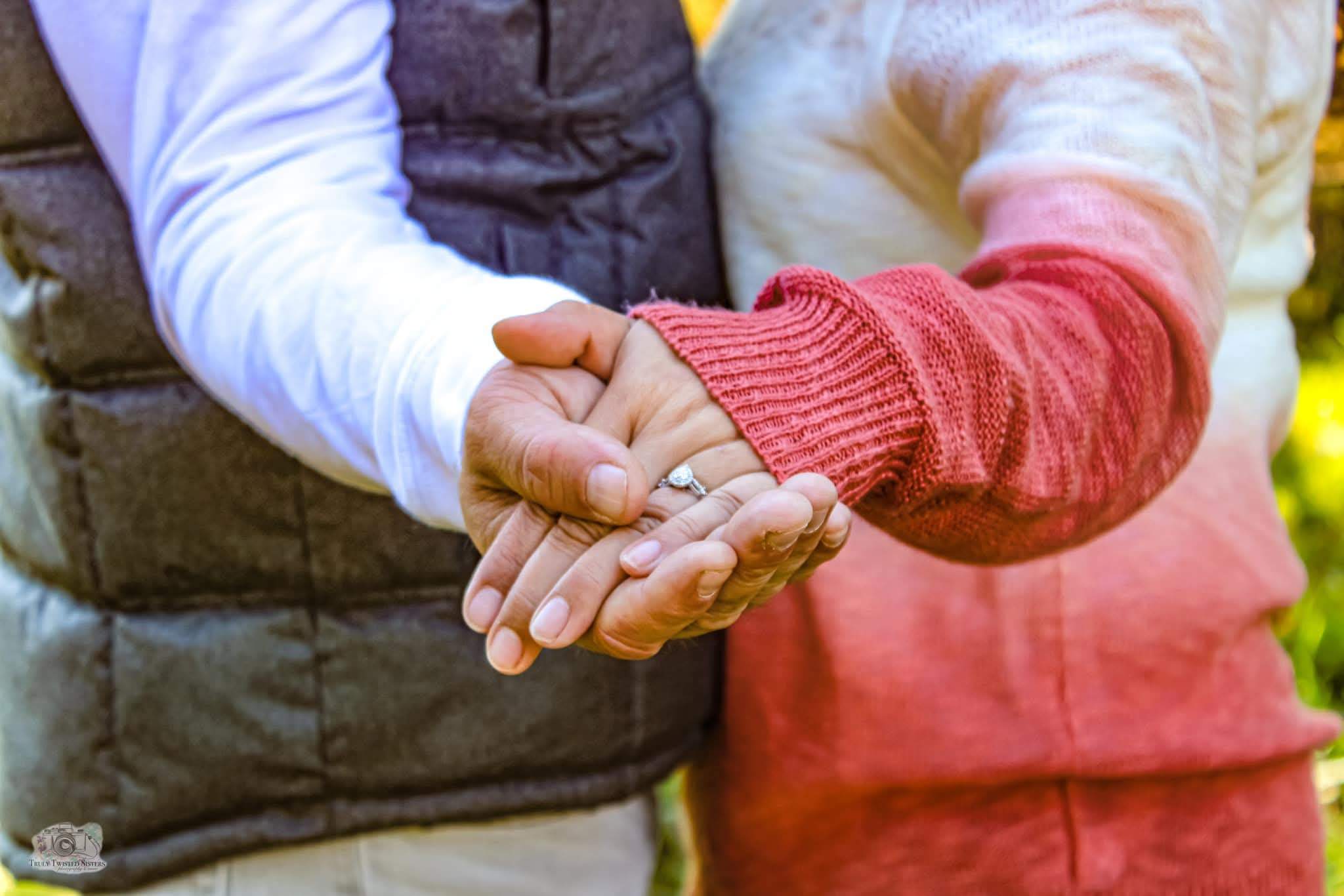 Couple holding hands, engagement ring catching the light against warm fall foliage