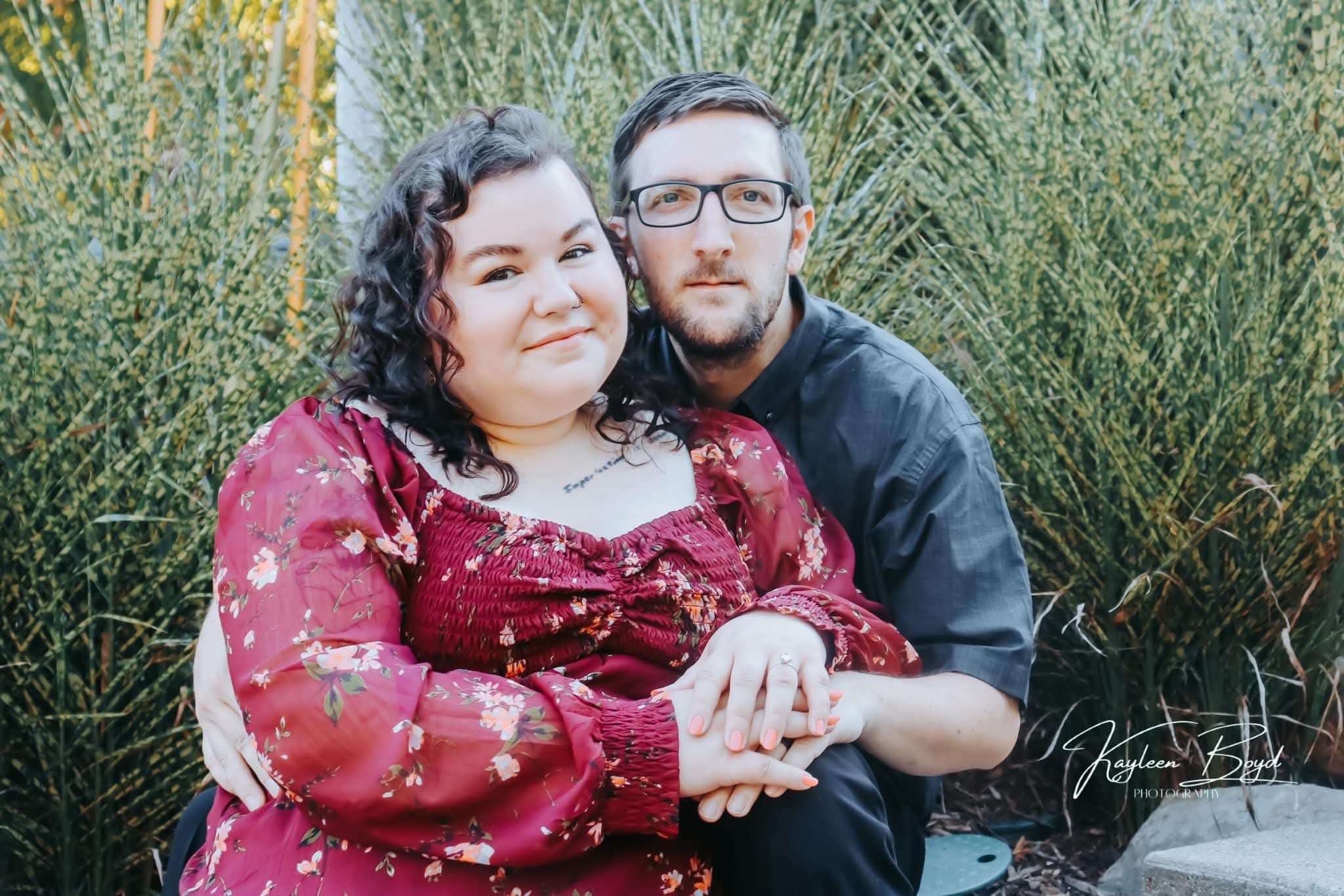 Couple seated together in front of ornamental grass, woman in burgundy floral blouse, warm natural light
