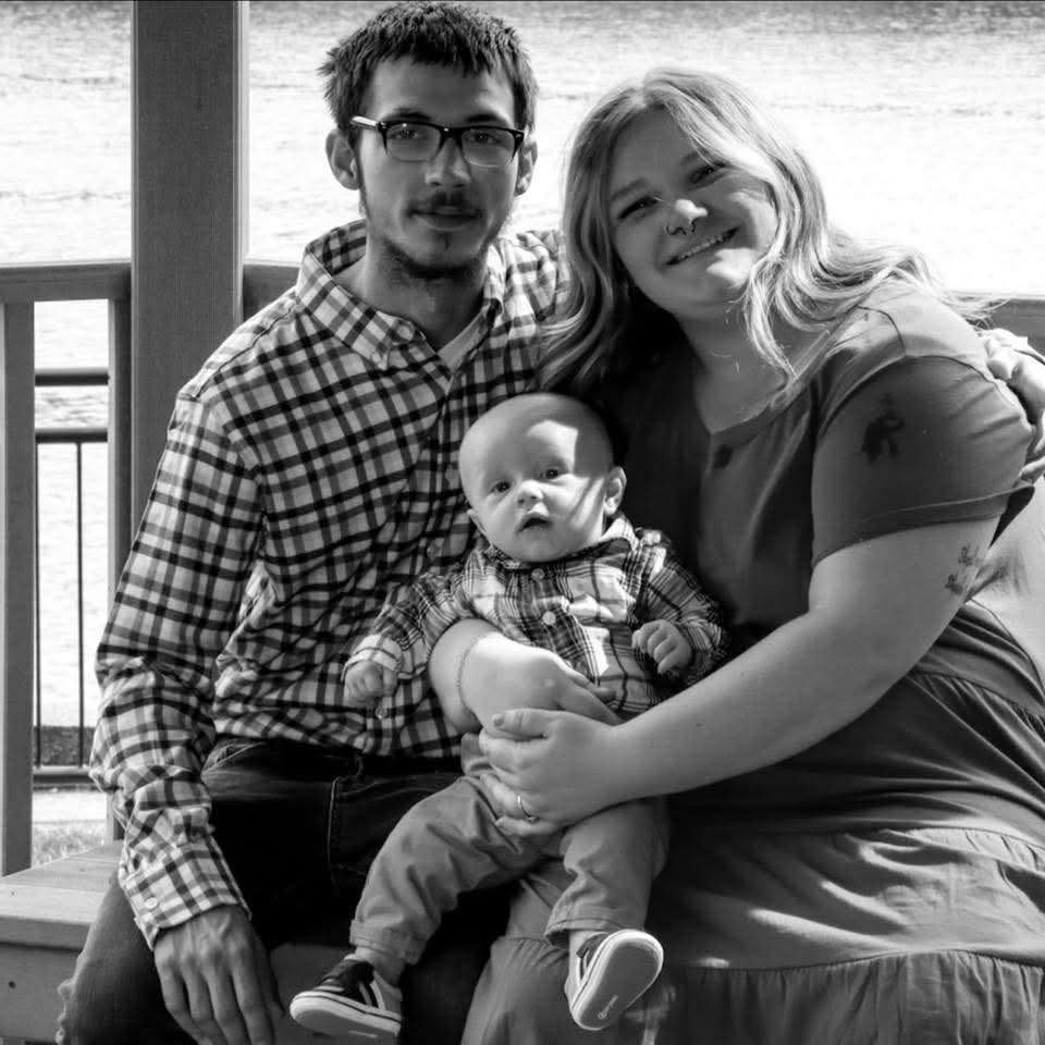 Young couple seated on a deck together holding their newborn baby, black and white portrait