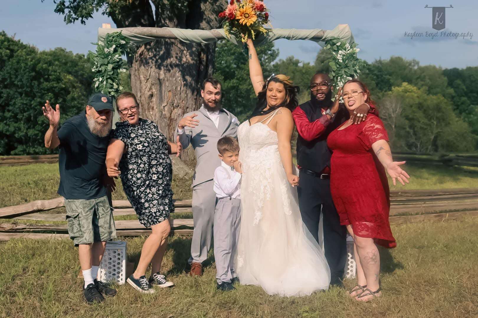 Wedding party and family celebrating together under a floral arch, pure joy