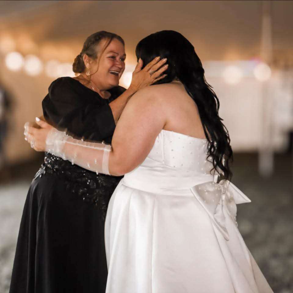 Bride and mother sharing an emotional dance at the reception, warm string lights behind them